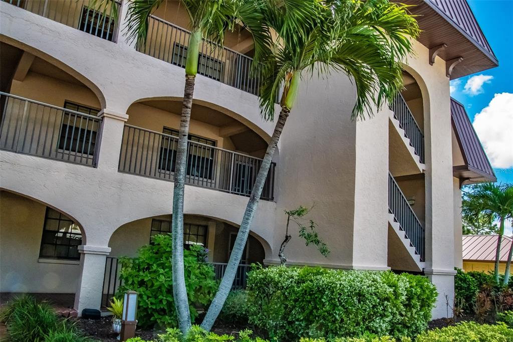 A multi-story apartment building exterior features arched balconies, metal railings, and tall palm trees — 23465 HARBORVIEW ROAD UNIT 245, PUNTA GORDA, FL