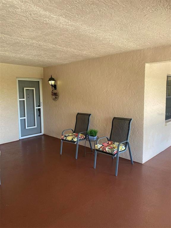 A covered porch features a gray front door, two outdoor chairs, and a wall-mounted light — 23465 HARBORVIEW ROAD UNIT 245, PUNTA GORDA, FL
