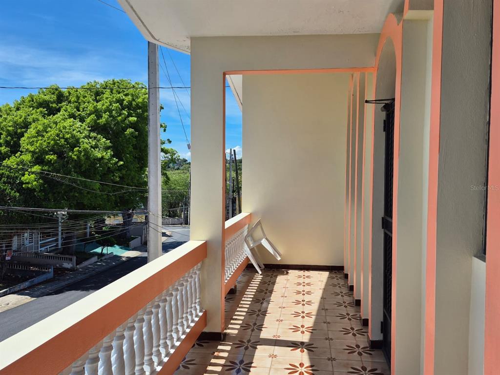 A covered balcony with a white balustrade, patterned tile flooring, and a view of trees — #55A CALLE JOSÉ HERNANDEZ, ISABELA, PR
