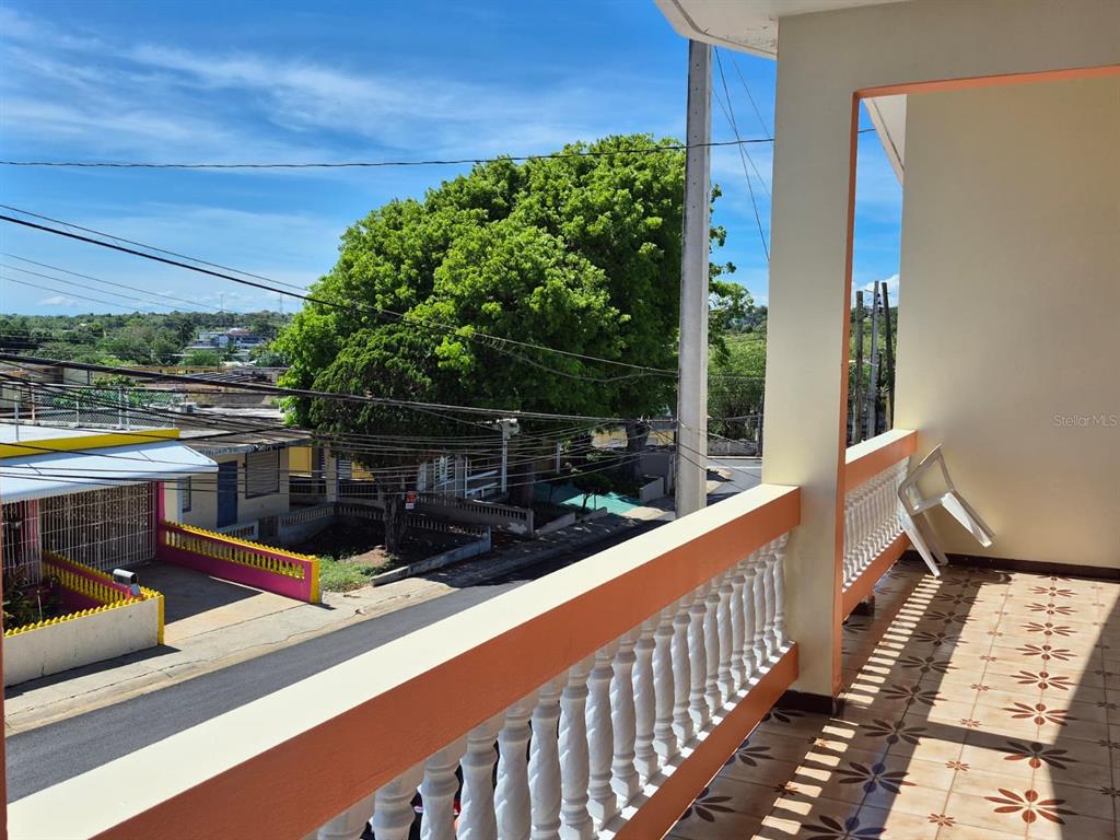 A balcony with a white balustrade overlooks a street with houses and a large tree — #55A CALLE JOSÉ HERNANDEZ, ISABELA, PR