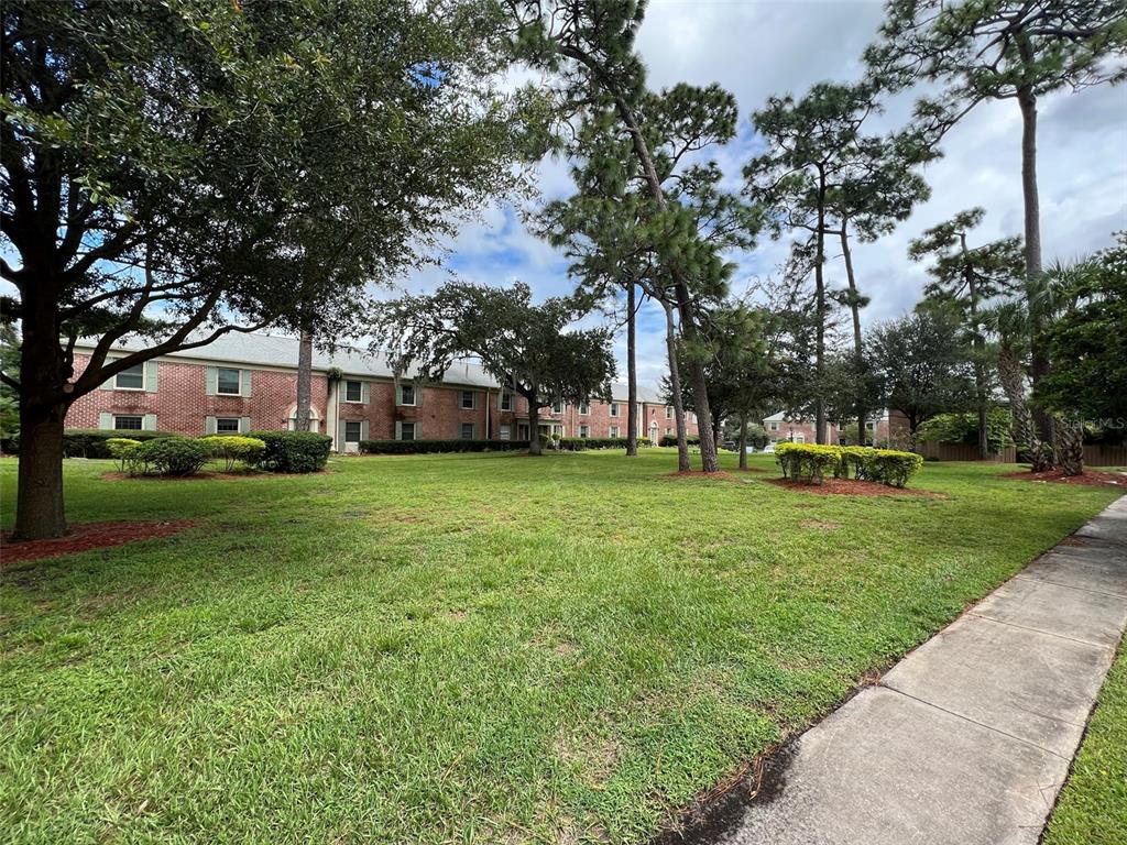 A two-story brick apartment building sits behind a large grassy lawn with mature trees — 524 GEORGETOWN DRIVE UNIT B, CASSELBERRY, FL