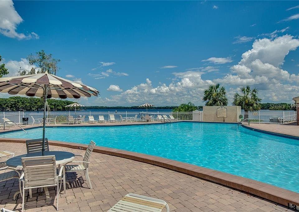 A swimming pool with lounge chairs and umbrellas overlooks a lake under a blue sky — 524 GEORGETOWN DRIVE UNIT B, CASSELBERRY, FL