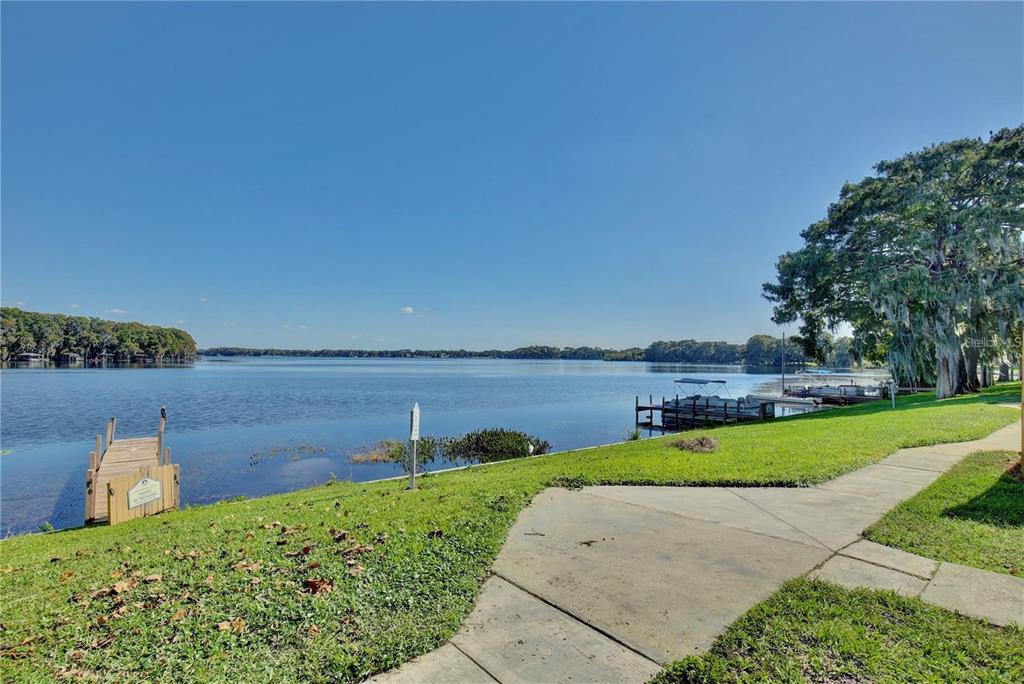 A concrete walkway leads toward a wooden dock on a lake under a clear sky — 524 GEORGETOWN DRIVE UNIT B, CASSELBERRY, FL