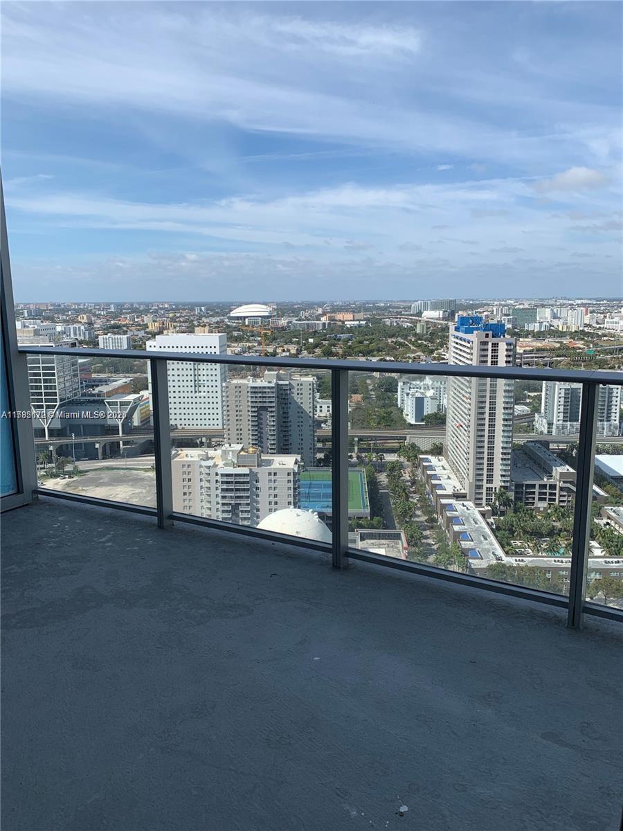 A high-rise balcony overlooks a dense urban cityscape with several tall buildings and a stadium — 851 NE 1st Ave # 3002, Miami FL 33132, MIAMI, FL