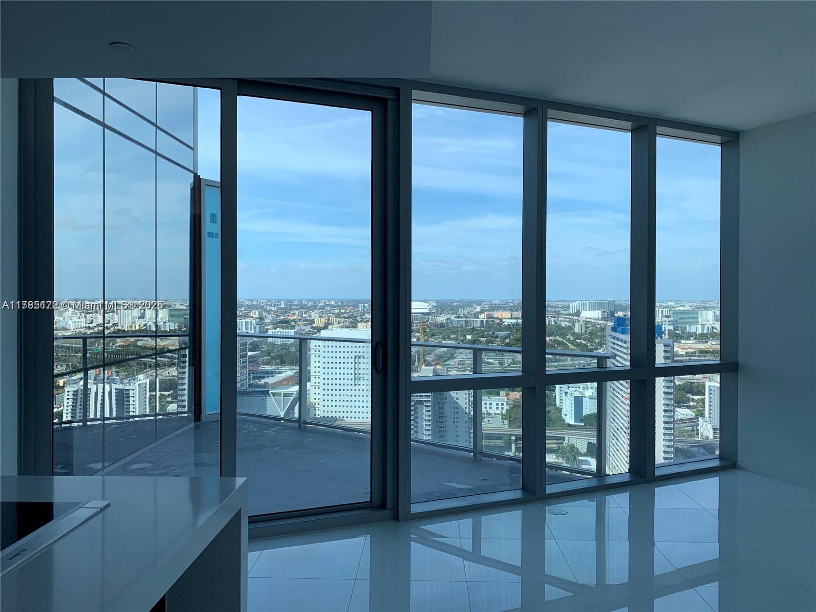 A modern room with floor-to-ceiling windows overlooking a city skyline and a balcony — 851 NE 1st Ave # 3002, Miami FL 33132, MIAMI, FL