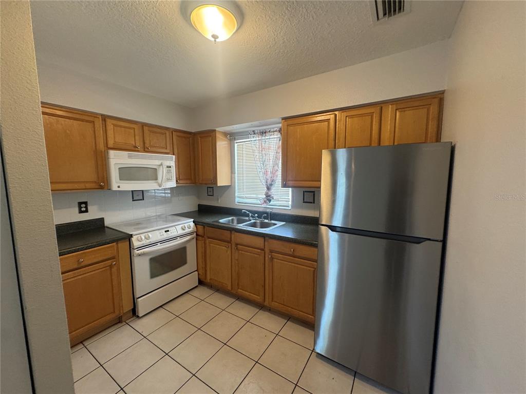 A kitchen with wood cabinets, stainless steel refrigerator, white stove, and tiled flooring — 3607 W IDLEWILD AVENUE UNIT 501, TAMPA, FL
