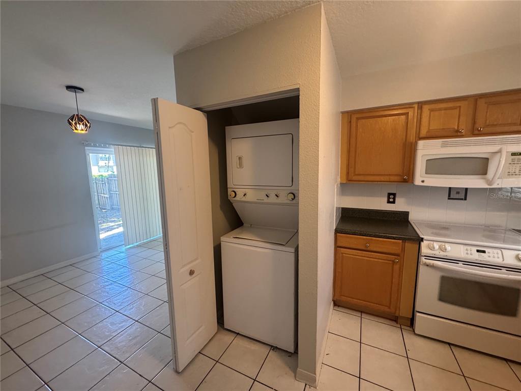 A kitchen features a stacked washer and dryer, wooden cabinets, and a tiled floor — 3607 W IDLEWILD AVENUE UNIT 501, TAMPA, FL