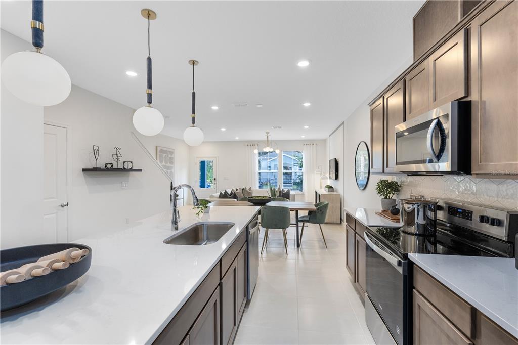 A modern kitchen features a white quartz island, dark wood cabinets, and stainless steel appliances — 11462 NONA SOUND STREET, ORLANDO, FL