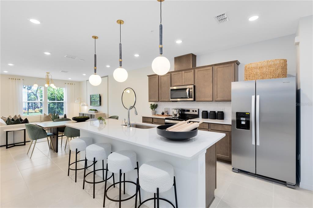 A modern kitchen features a white island with bar stools, stainless appliances, and wooden cabinetry — 11462 NONA SOUND STREET, ORLANDO, FL
