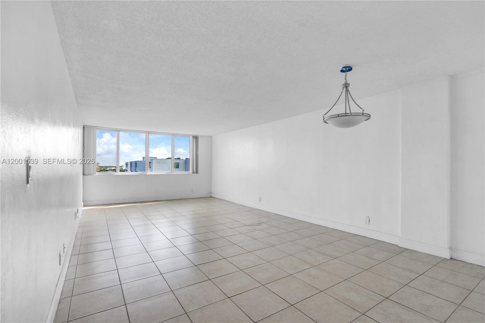An empty room features white walls, light-colored tile flooring, and a hanging pendant light — 9143 SW 77th Ave # B710, Miami FL 33156, MIAMI, FL