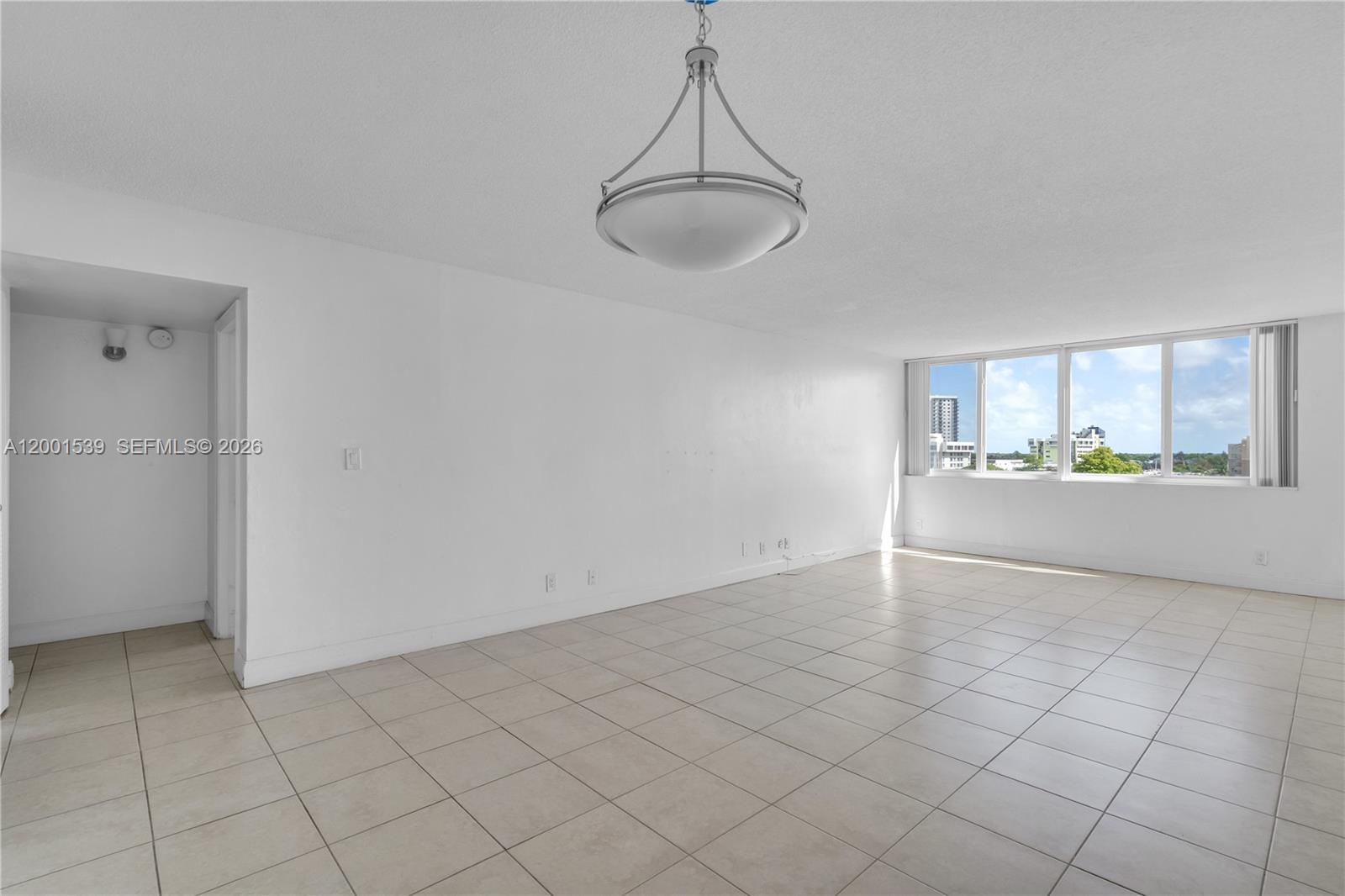 An empty room features white walls, light-colored tile flooring, a central pendant light, and windows — 9143 SW 77th Ave # B710, Miami FL 33156, MIAMI, FL