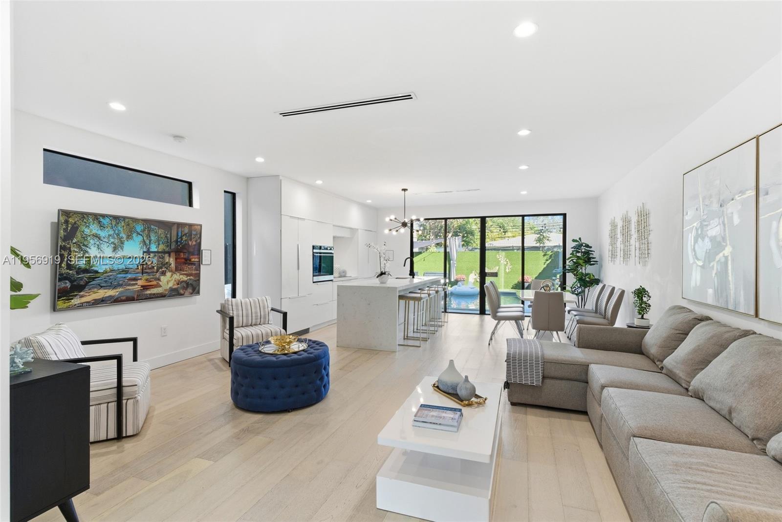 A modern open-concept living room and kitchen featuring light wood floors and a backyard pool — 255 NW 39th St, Miami FL 33127, MIAMI, FL