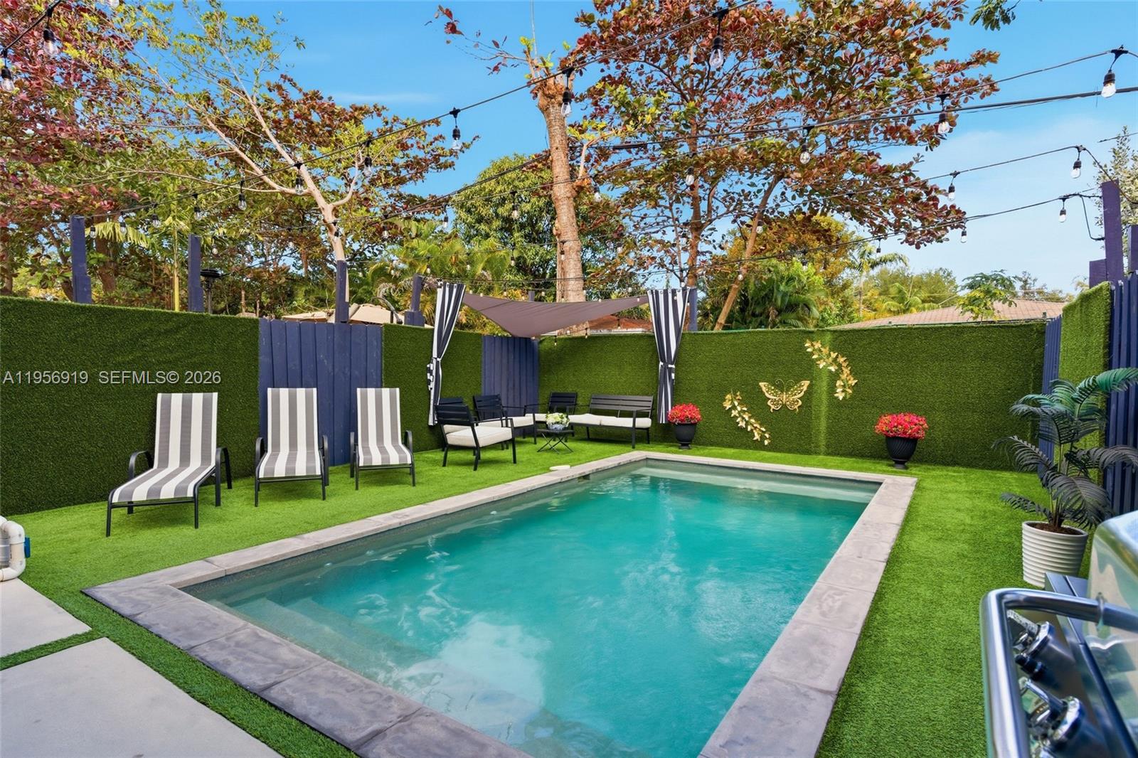 A rectangular swimming pool is surrounded by artificial turf, lounge chairs, and a privacy fence — 255 NW 39th St, Miami FL 33127, MIAMI, FL