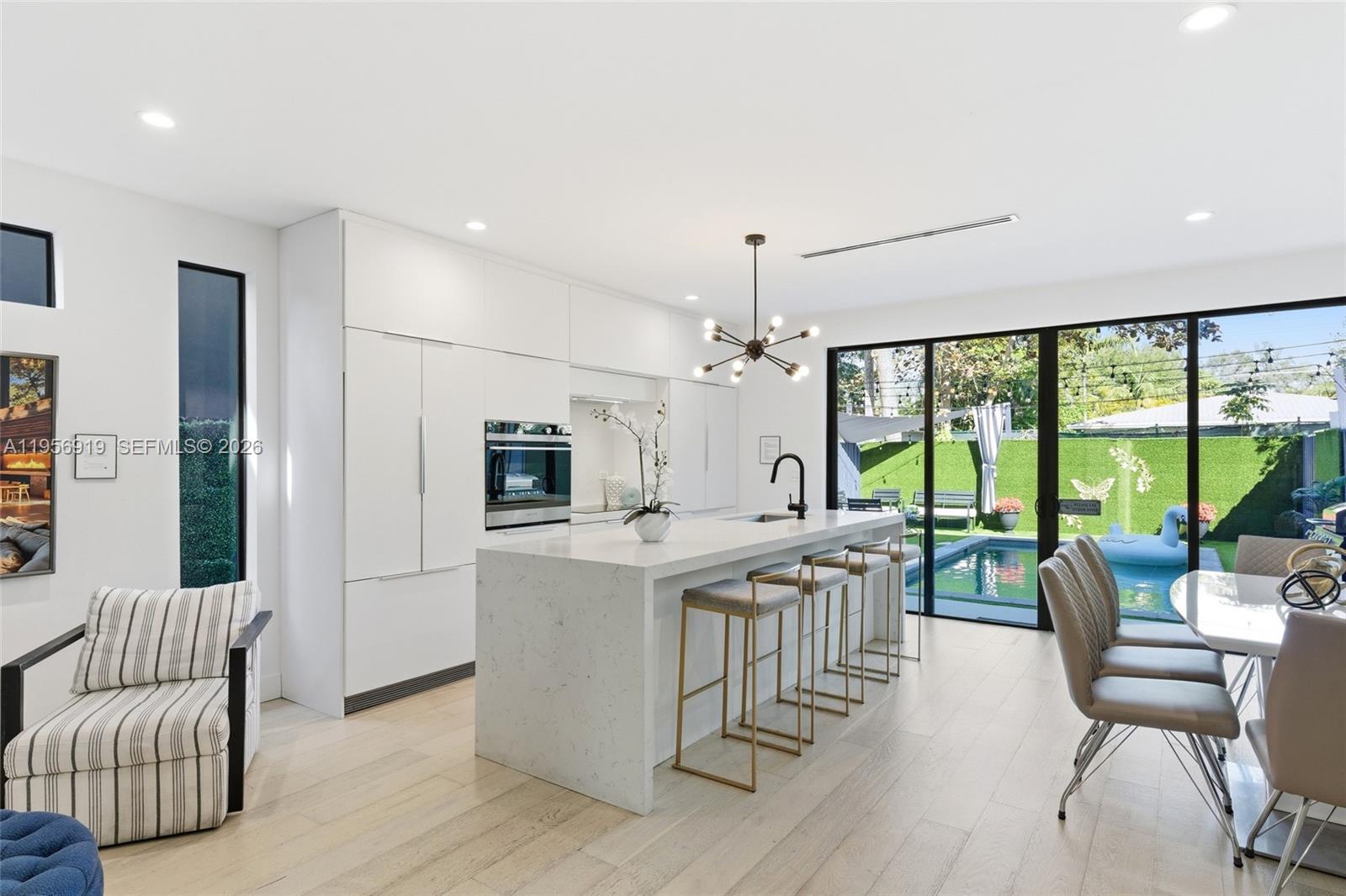 A modern kitchen features white cabinetry, a marble island with bar stools, and pool views — 255 NW 39th St, Miami FL 33127, MIAMI, FL