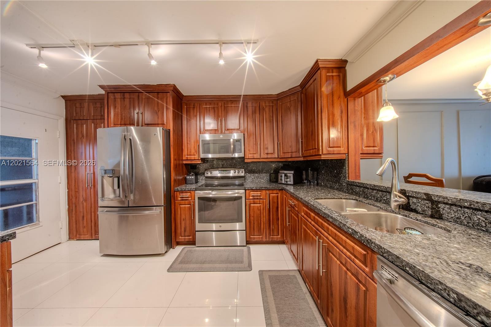 A kitchen features dark wood cabinets, granite countertops, stainless steel appliances, and white tile flooring — 1660 NE 191st St # 1, Miami FL 33179, MIAMI, FL