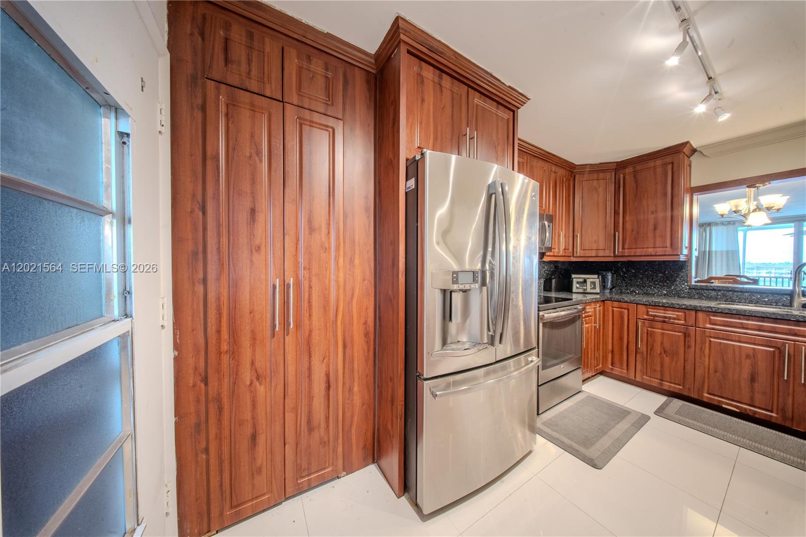 A kitchen features wood cabinets, stainless steel appliances, and white tile flooring — 1660 NE 191st St # 1, Miami FL 33179, MIAMI, FL
