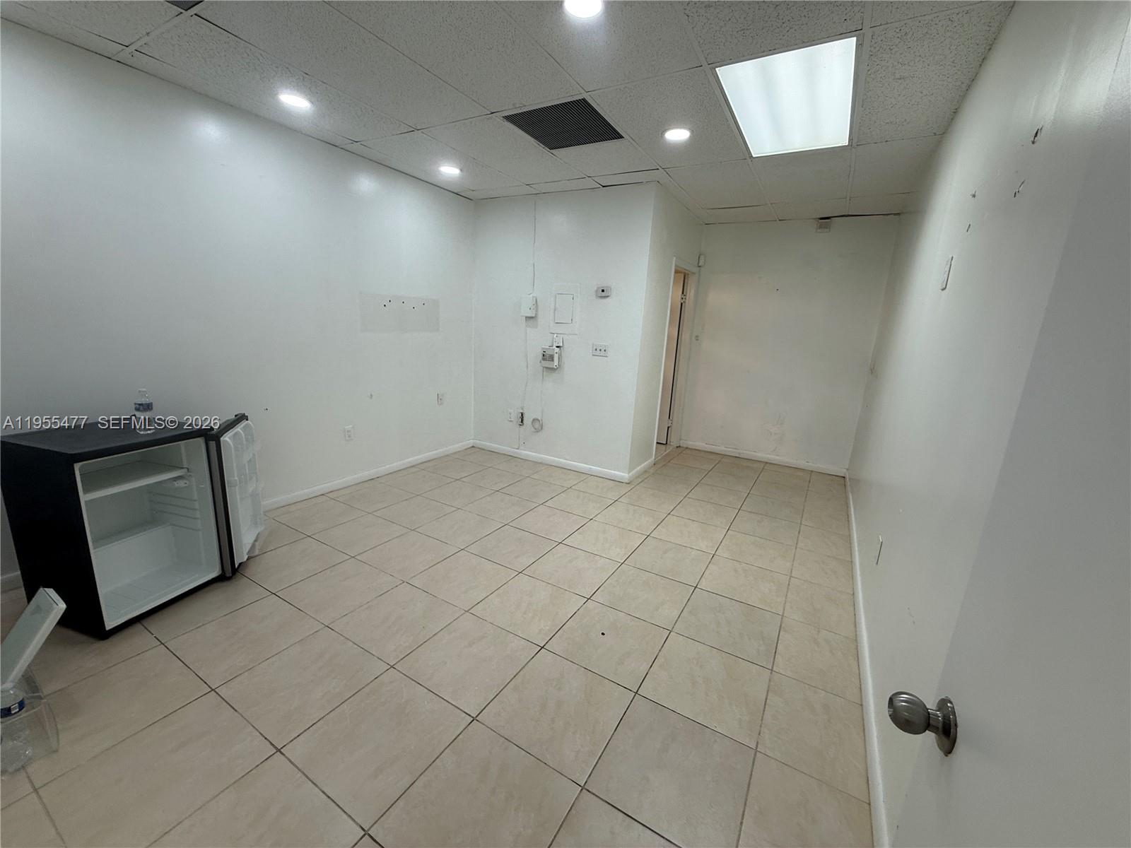 A small, empty room features white walls, beige tile flooring, and a mini refrigerator — 10509 SW 40th St # 10509, Miami FL 33165, MIAMI, FL