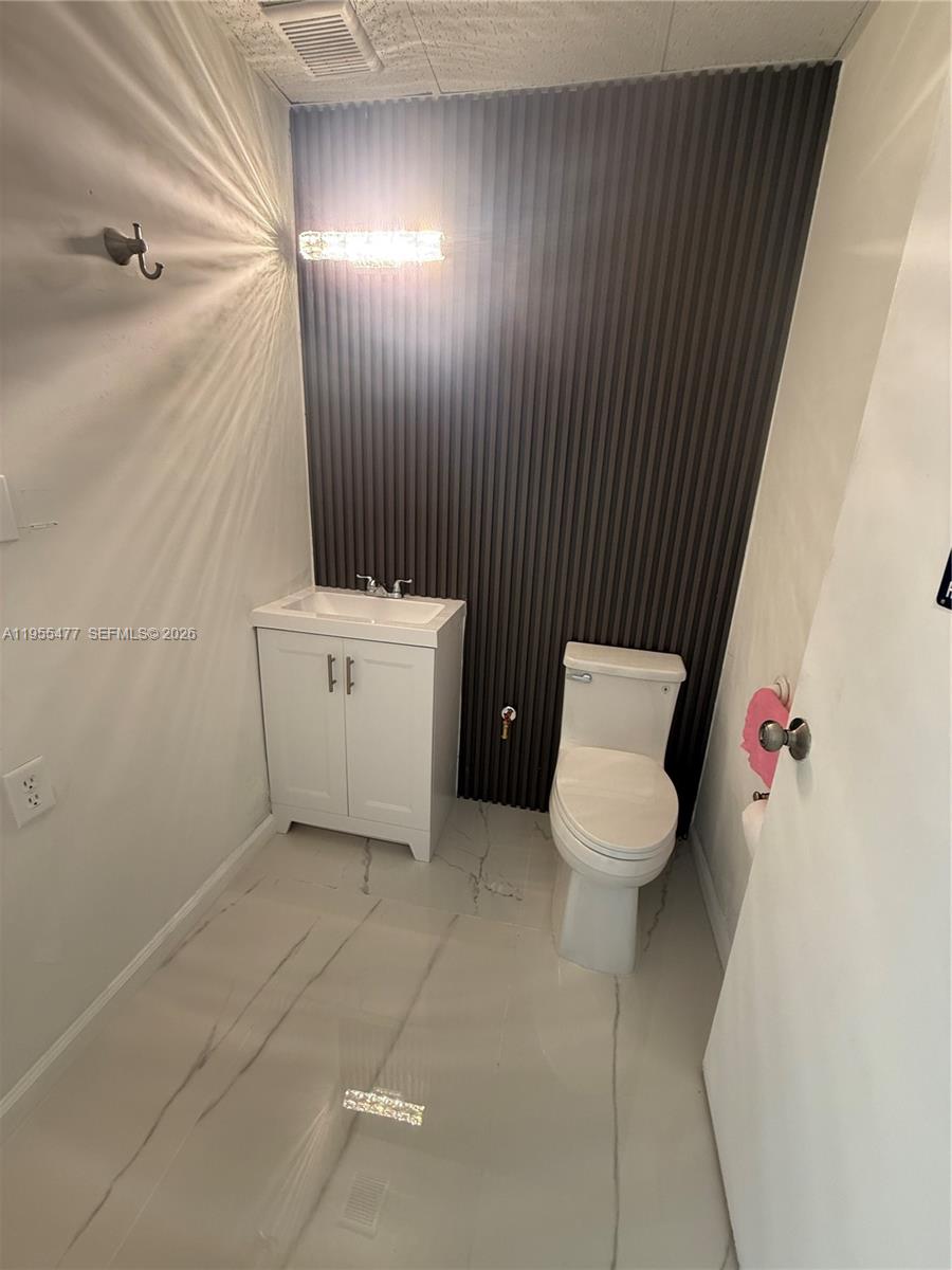 A small bathroom features a white vanity, a toilet, and a dark vertical-slatted accent wall — 10509 SW 40th St # 10509, Miami FL 33165, MIAMI, FL