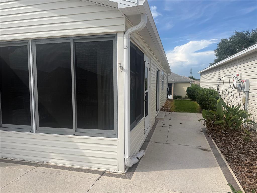 A screened-in porch with white siding and a concrete walkway along the side exterior — 484 HILDALGO DRIVE, LADY LAKE, FL