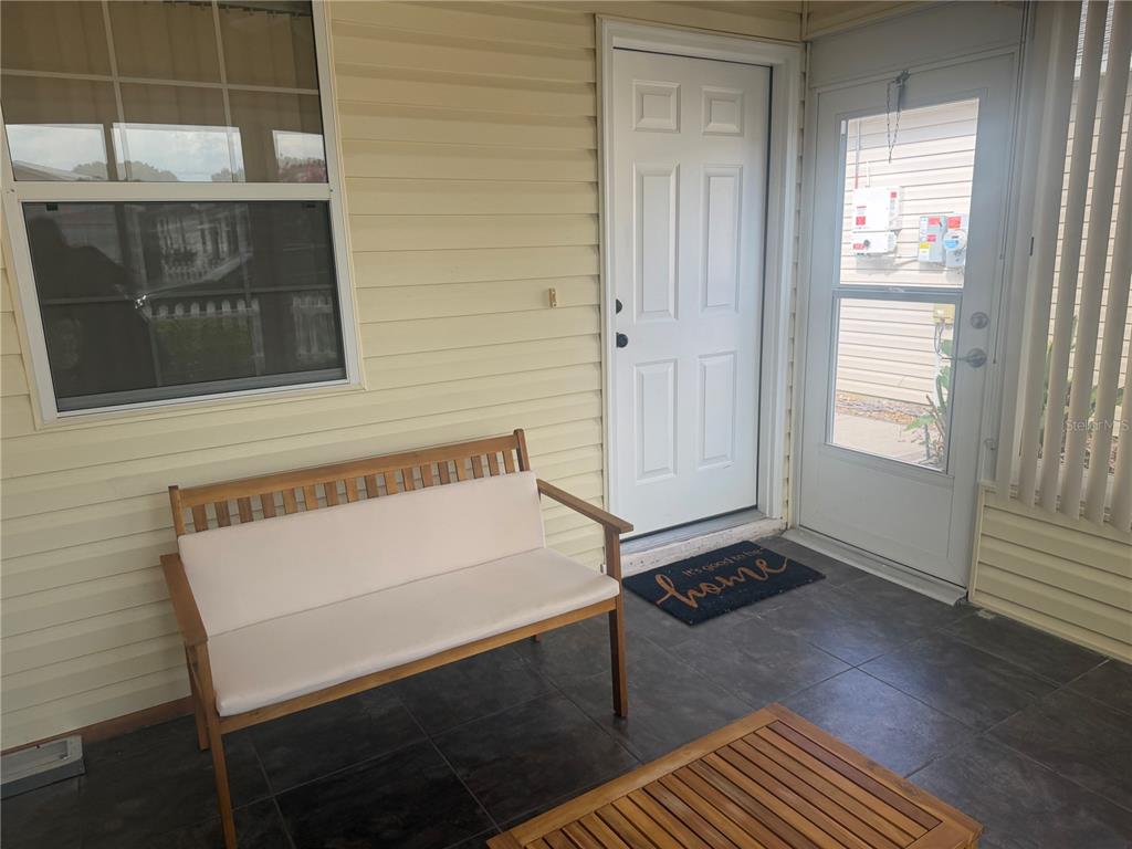 A covered porch features a wooden bench, tiled flooring, a white door, and a screen door — 484 HILDALGO DRIVE, LADY LAKE, FL