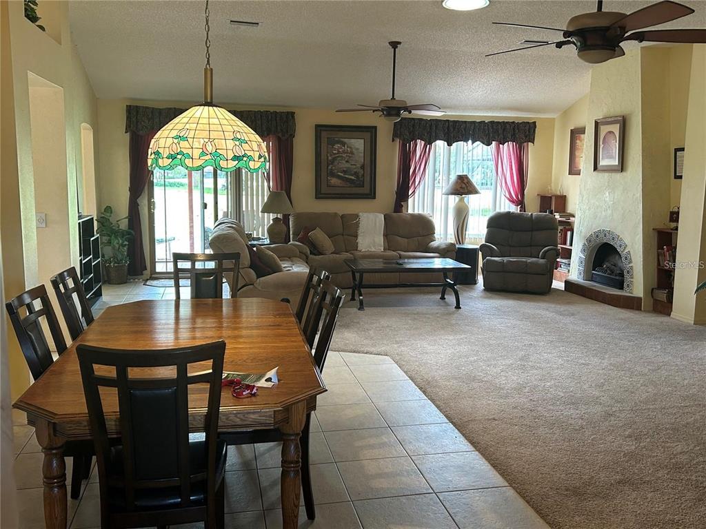 A dining area with a wooden table transitions into a carpeted living room with a fireplace — 867 CORTEZ AVENUE, THE VILLAGES, FL
