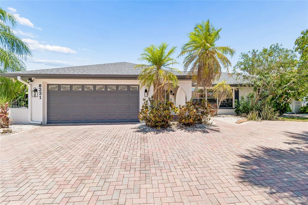A single-story house with a gray garage door, palm trees, and a brick paver driveway — 6331 COCOA LANE, APOLLO BEACH, FL