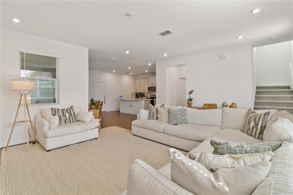 A bright living room features a large sectional sofa, a white armchair, and an open kitchen — 11356 SUNSAIL AVENUE, ORLANDO, FL