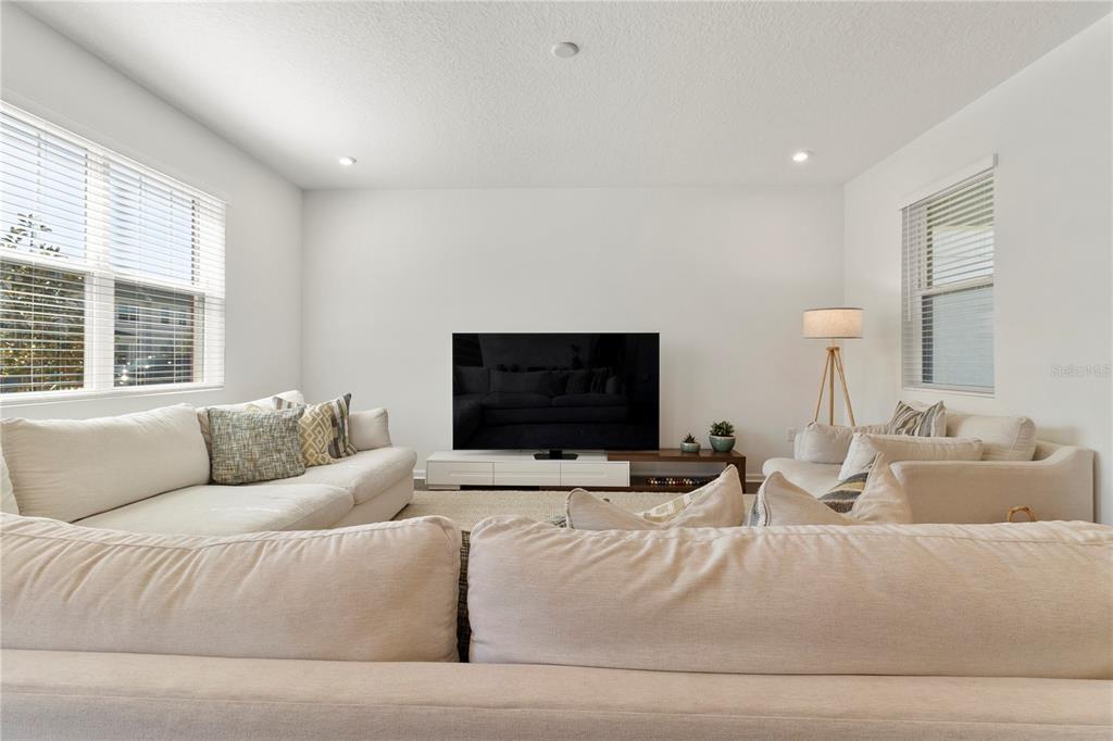 A living room features white walls, light-colored sofas, a television on a stand, and windows — 11356 SUNSAIL AVENUE, ORLANDO, FL