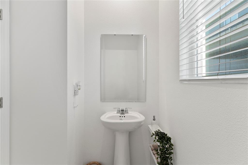 A small bathroom features a white pedestal sink, a wall-mounted mirror, and a window — 11356 SUNSAIL AVENUE, ORLANDO, FL