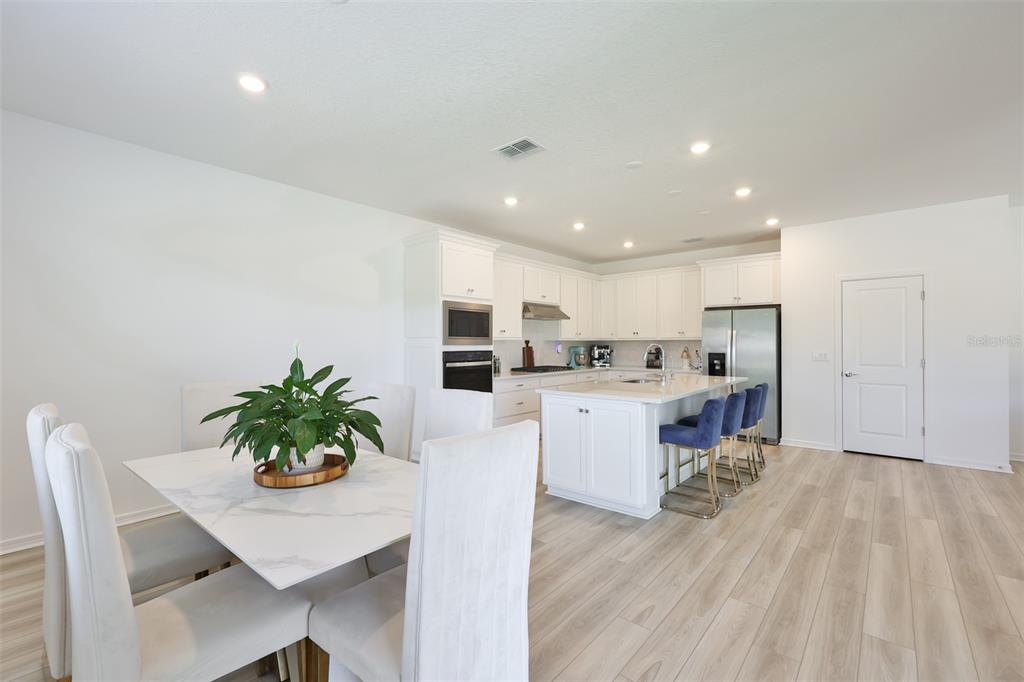 A bright kitchen features white cabinetry, a center island with bar stools, and a dining area — 3070 FOREST MEADOW AVENUE, VALRICO, FL