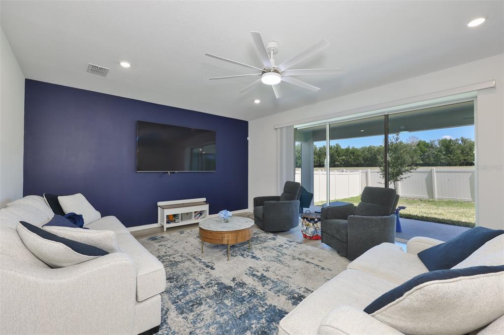 A living room features a navy accent wall, white sofas, and a sliding glass door — 3070 FOREST MEADOW AVENUE, VALRICO, FL
