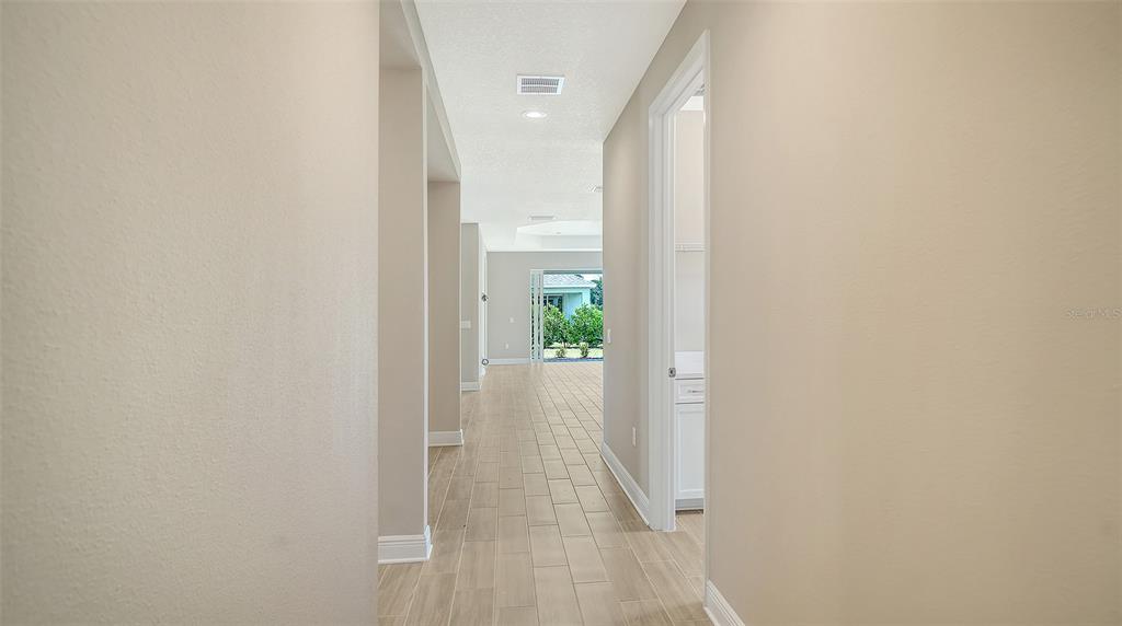 A hallway with light-colored walls and wood-look tile flooring leads toward an exterior view — 10026 CROSS RIVER TRAIL, PARRISH, FL