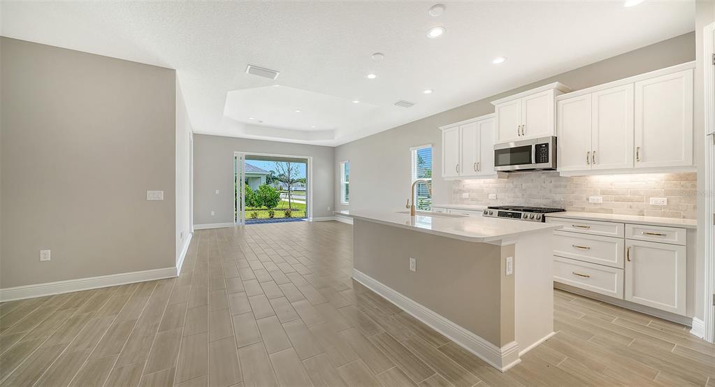 A modern kitchen with white cabinets, a central island, and tile flooring opens to a living area — 10026 CROSS RIVER TRAIL, PARRISH, FL
