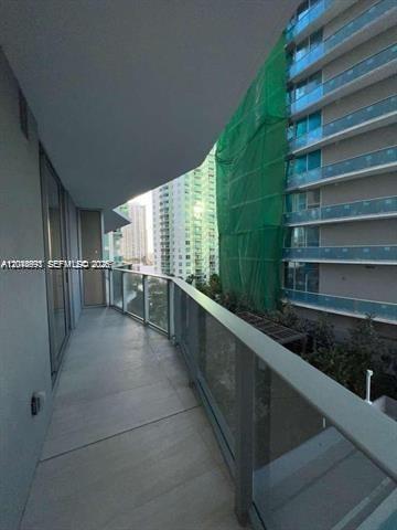A balcony with a glass railing overlooks a neighboring high-rise building covered in green netting — 77 SE 5th St # 1605, Miami FL 33131, MIAMI, FL