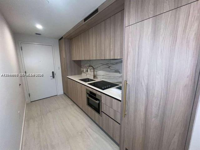 A modern kitchen features wood-grain cabinetry, a marble backsplash, and integrated stainless steel appliances — 77 SE 5th St # 1605, Miami FL 33131, MIAMI, FL