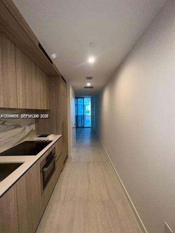 A narrow kitchen features light wood cabinetry, a marble backsplash, and a stainless steel oven — 77 SE 5th St # 1605, Miami FL 33131, MIAMI, FL