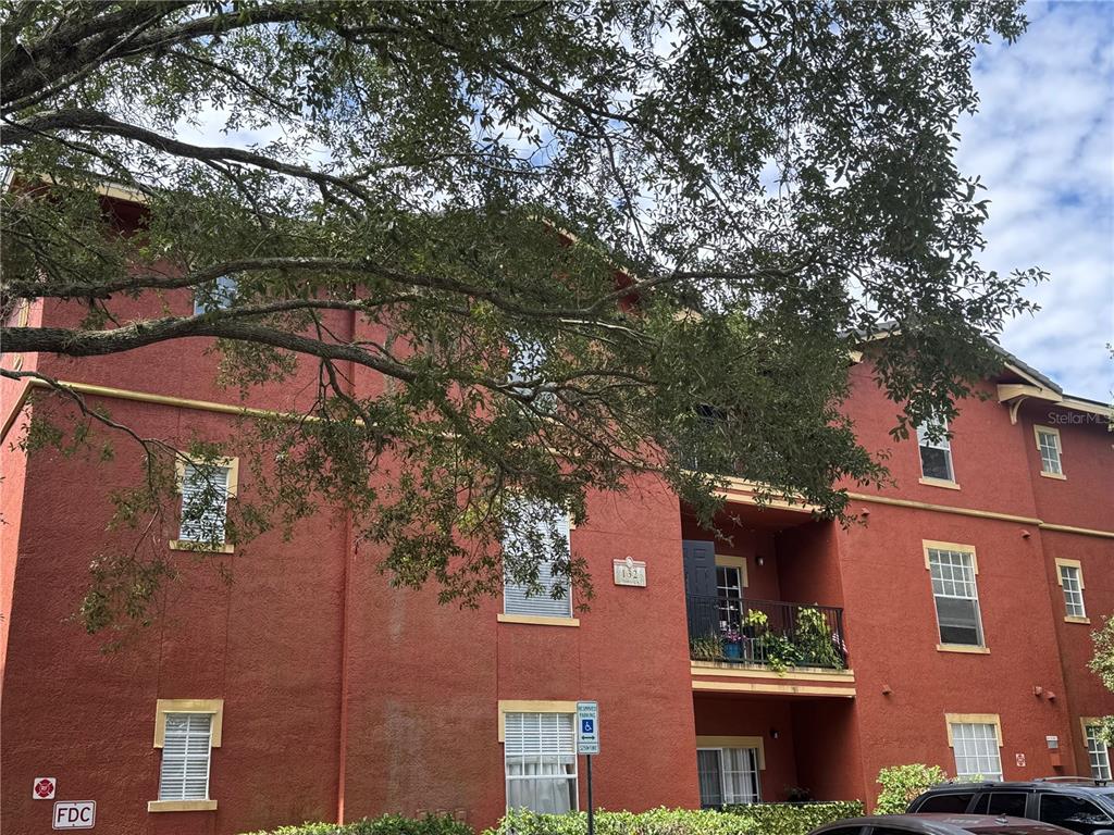 The exterior of a three-story red apartment building features a balcony and a fire connection — 132 VISTA VERDI CIRCLE UNIT 136, LAKE MARY, FL