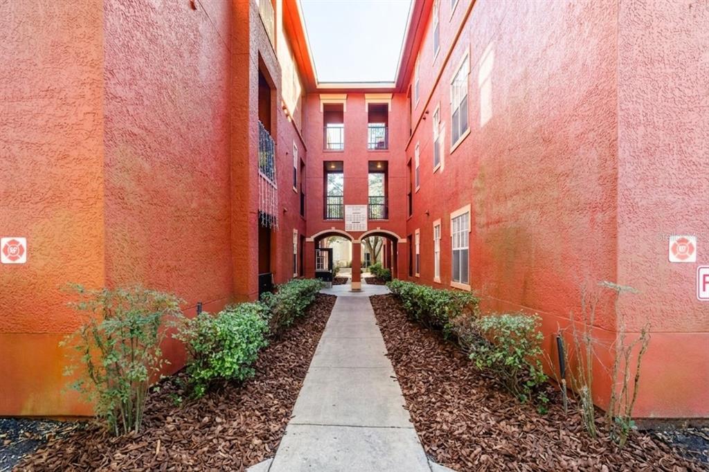 A concrete walkway leads between two red apartment buildings with balconies and landscaping — 132 VISTA VERDI CIRCLE UNIT 136, LAKE MARY, FL