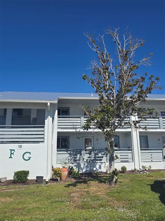 A two-story apartment building with gray railings, a metal roof, and a tree in front — 6800 PLACIDA ROAD UNIT 167, ENGLEWOOD, FL