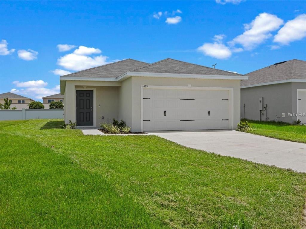 A single-story house with a beige exterior, a two-car garage, and a dark front door — 1403 MADISON CIRCLE, HAINES CITY, FL