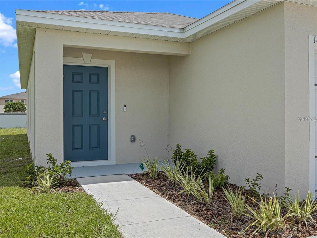 A blue front door is set into the recessed entryway of a beige stucco house — 1403 MADISON CIRCLE, HAINES CITY, FL