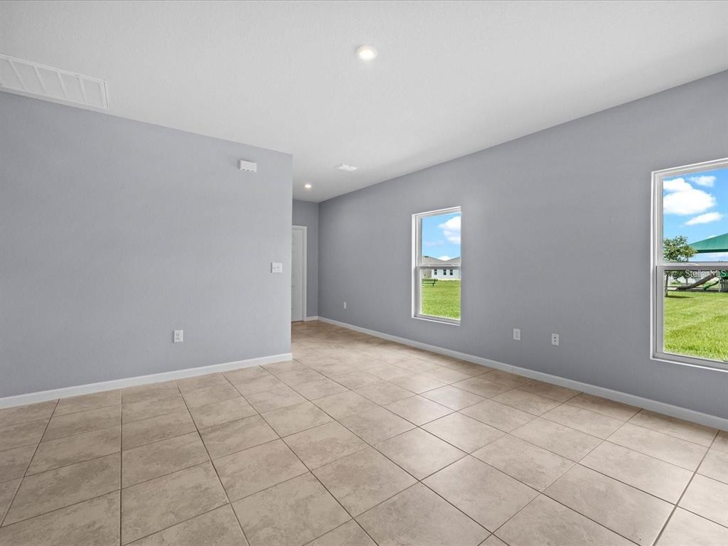An empty room with light gray walls, tan tile flooring, and two windows — 1403 MADISON CIRCLE, HAINES CITY, FL
