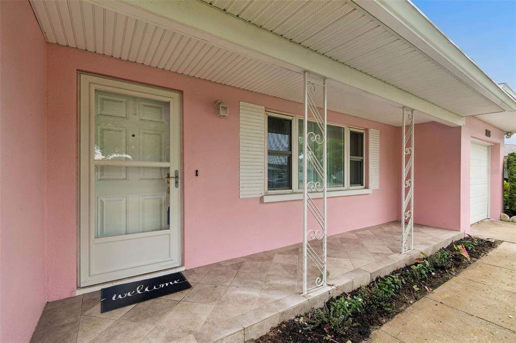 A pink exterior house features a covered front porch with tiled flooring and white columns — 808 WOODLEY ROAD, CLEARWATER, FL
