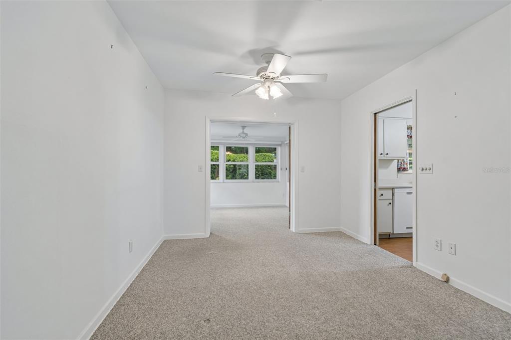 A carpeted room with a ceiling fan leads to an adjacent space with large windows — 808 WOODLEY ROAD, CLEARWATER, FL