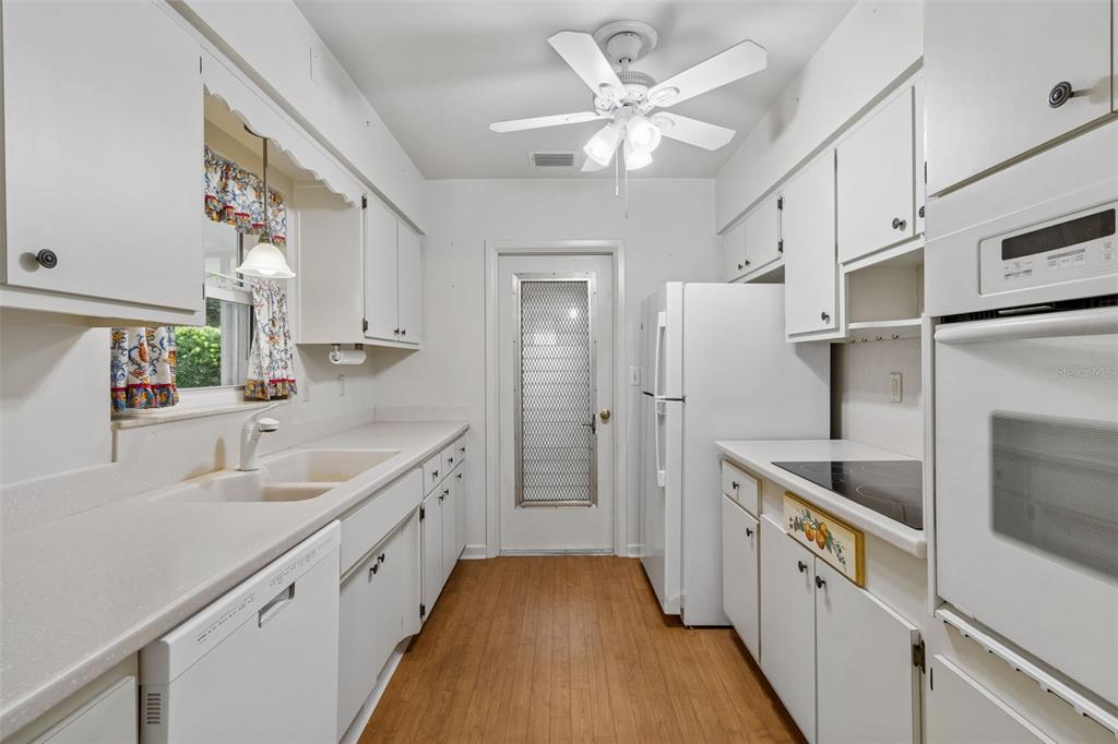 A galley kitchen features white cabinets, white appliances, a double sink, and wood-look flooring — 808 WOODLEY ROAD, CLEARWATER, FL