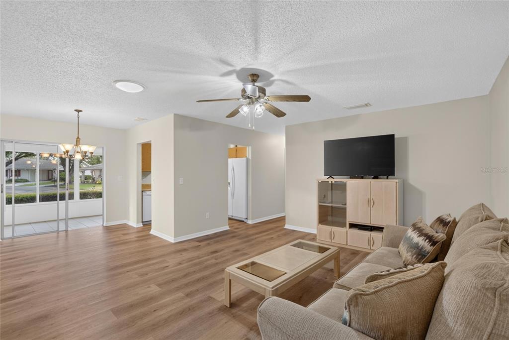 A living room features wood-look flooring, a ceiling fan, a television, and a sliding door — 2202 HORSHAM PLACE, SUN CITY CENTER, FL