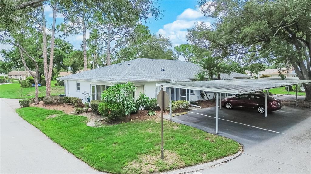 A white single-story building with a metal carport and a maroon car parked underneath — 2202 HORSHAM PLACE, SUN CITY CENTER, FL