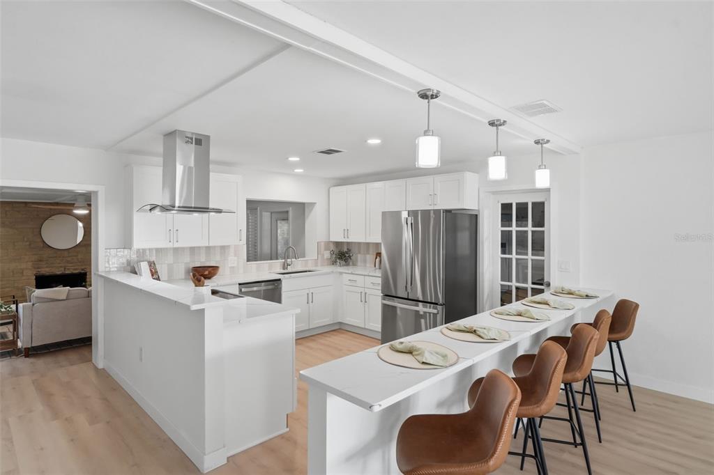 A modern kitchen features white cabinetry, stainless steel appliances, and a breakfast bar with stools — 1360 IRVING AVENUE, CLEARWATER, FL