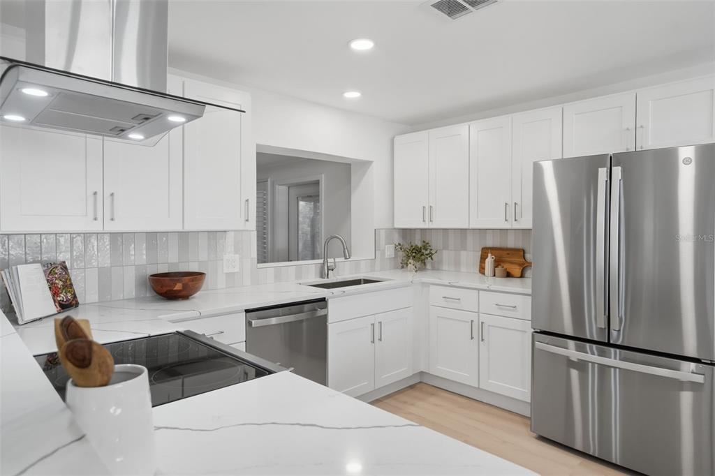 A modern kitchen features white cabinets, stainless steel appliances, and white marble-look countertops — 1360 IRVING AVENUE, CLEARWATER, FL