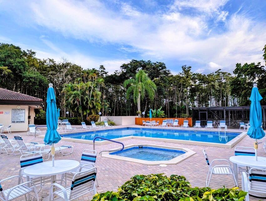 An outdoor swimming pool and hot tub surrounded by lounge chairs and blue umbrellas — 21362 Juego Circle # 33f, Boca Raton FL 33433, BOCA RATON, FL
